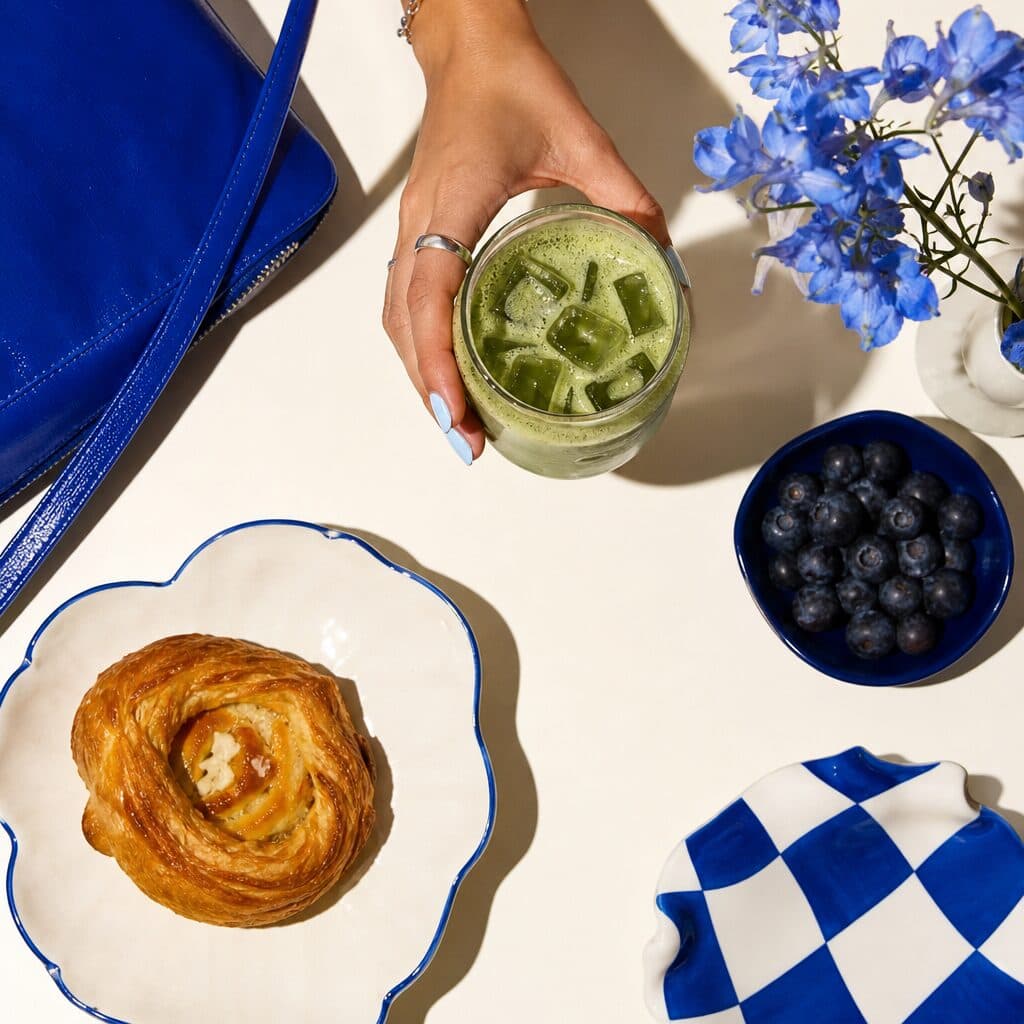 A danish on the scalloped plate, an iced matcha in hand and blueberries alongside