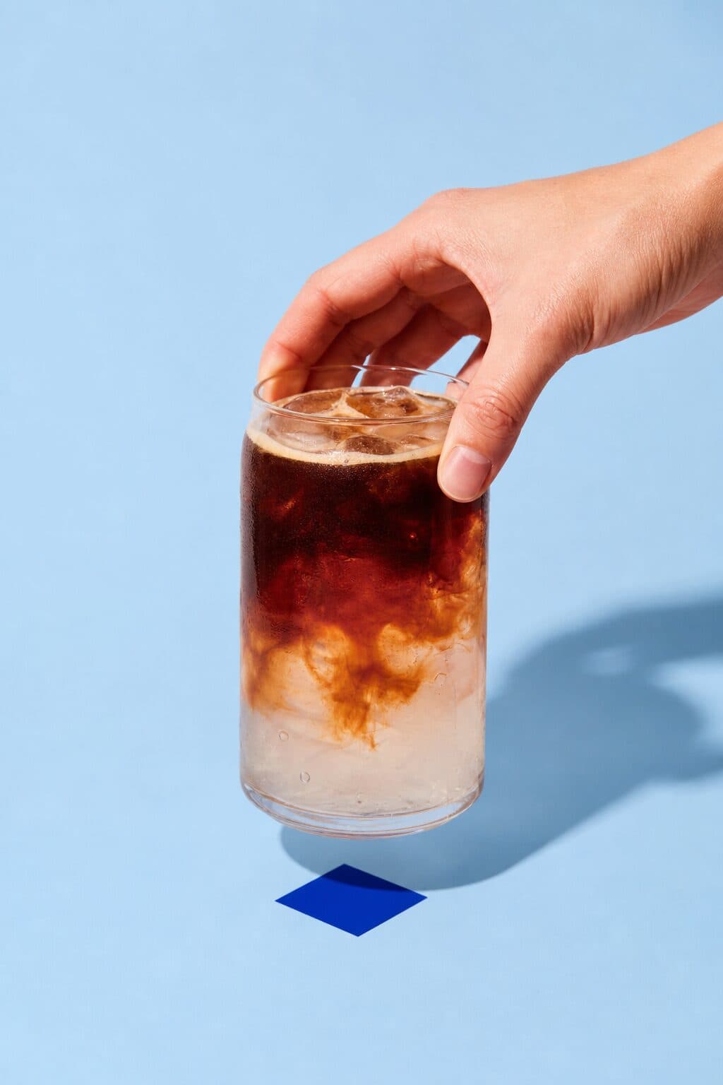 Iced coffee in a can glass, condensation on, held above the blue tile